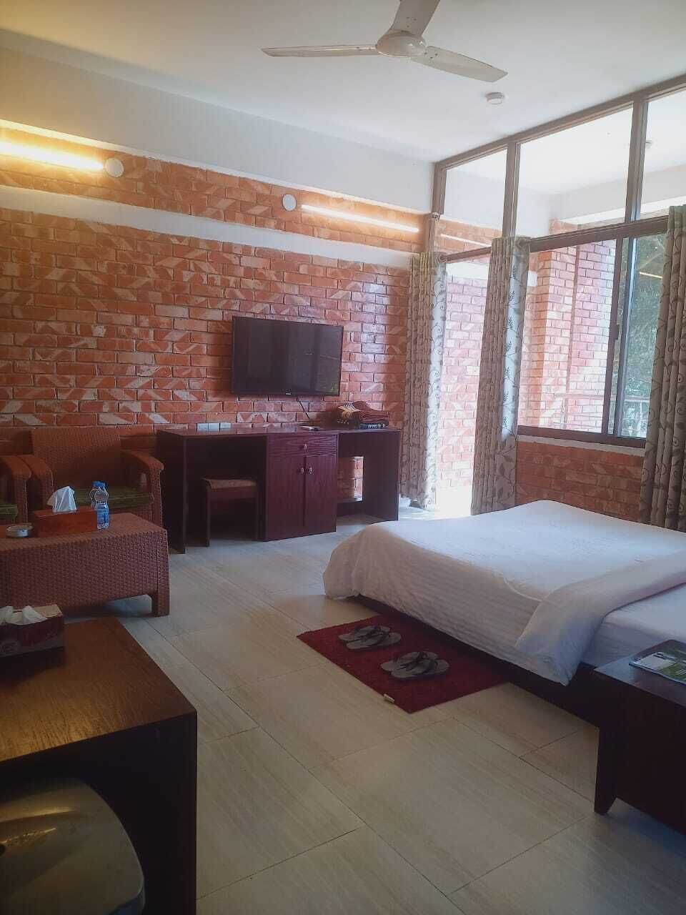 Camera d'albergo con parete in mattoni, televisione a schermo piatto, un letto, una scrivania e una finestra con tende.