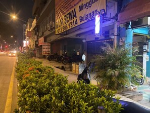 A building with a signboard advertising SEWA services, a parked motorcycle, and a well-maintained garden area with shrubs and a palm tree. - Global Inn Hostel (Kuala Lumpur)