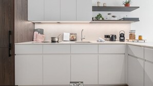 Una cucina moderna con mobili bianchi, forno integrato, lavello e macchina per il caffè. Ripiani sopra il bancone ospitano oggetti decorativi e piante.