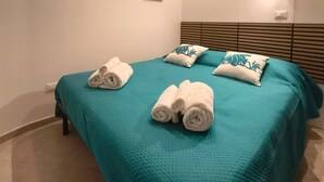 A neatly made bed with teal bedding and white towels, a wooden headboard, and three framed pictures on the wall. - The Calypso Mansion (Salerno)