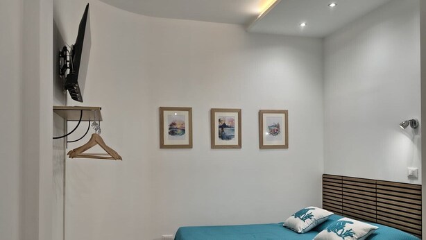 A modern bedroom with a teal bedspread, a wooden headboard, and a wall-mounted TV. There are three framed pictures on the wall, a wooden table with a plate of food, and a chair. - The Calypso Mansion (Salerno)