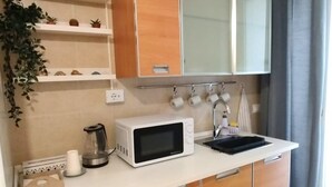 A modern kitchen with a microwave, kettle, and sink. There are wooden cabinets and a countertop with a plant. - The Calypso Mansion (Salerno)
