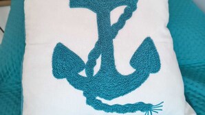 A pillow with a blue anchor design on a teal textured surface. - The Calypso Mansion (Salerno)