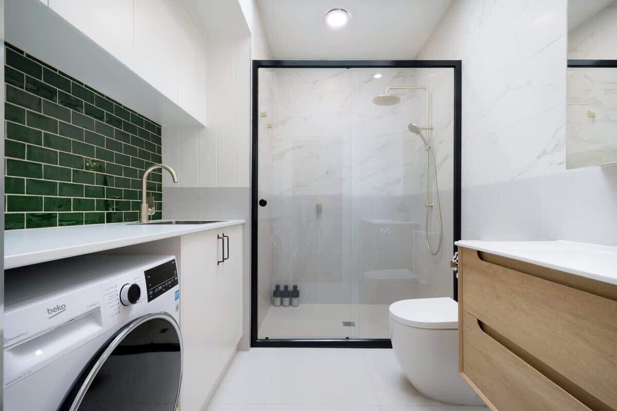 Une salle de bain moderne équipée d’un lave-linge, d’une douche à parois de verre et d’un meuble-lavabo en bois.