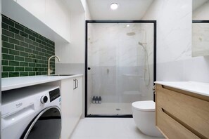 A modern bathroom with a washing machine, a glass-enclosed shower, and a wooden vanity.