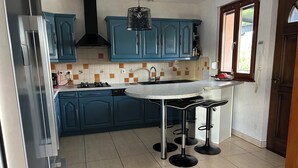Una cocina con gabinetes azules, un refrigerador de acero inoxidable, una campana extractora negra, un fregadero y una zona con taburetes de bar.