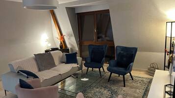 A modern living room with a sofa, two armchairs, a glass coffee table, and a rug.