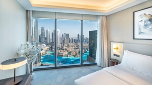Hotelkamer met groot raam en uitzicht over de stad, een bed, nachtkastje en lamp.