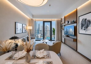 A modern hotel room with a dining area, a sofa, a TV, and a view of the cityscape.