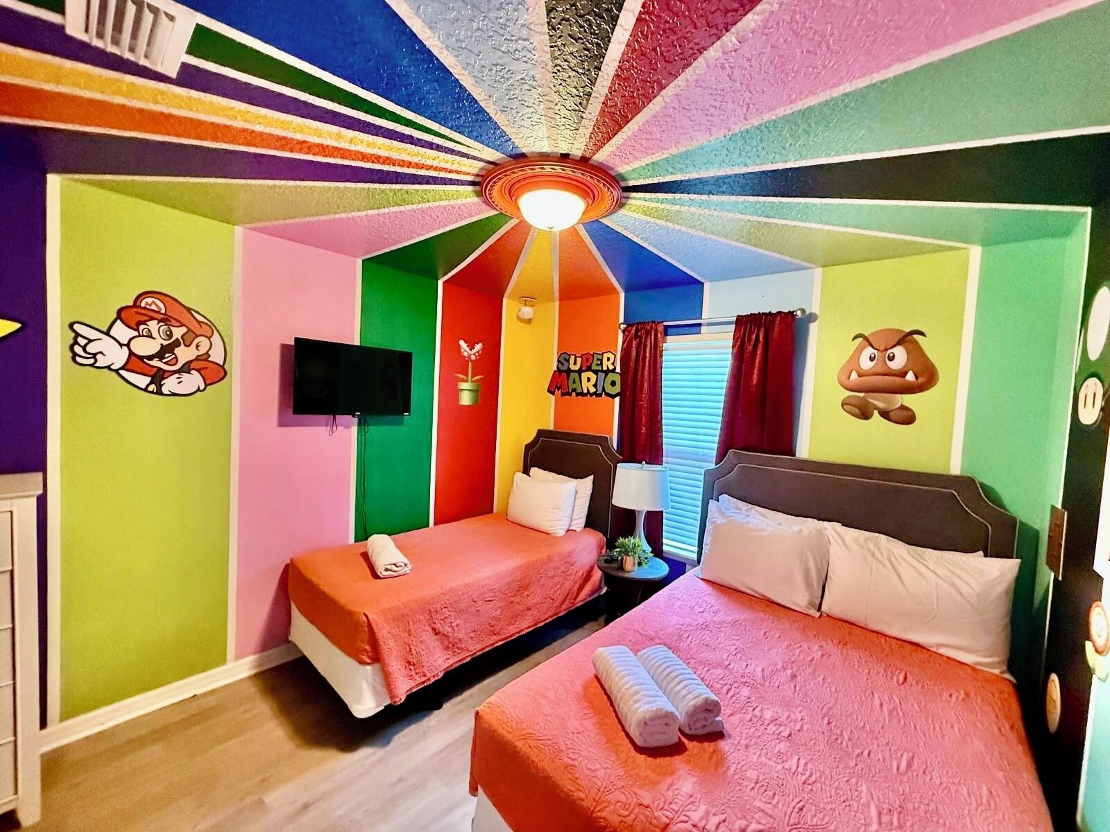 Une chambre aux couleurs vives, avec deux lits, un téléviseur et un ventilateur de plafond.