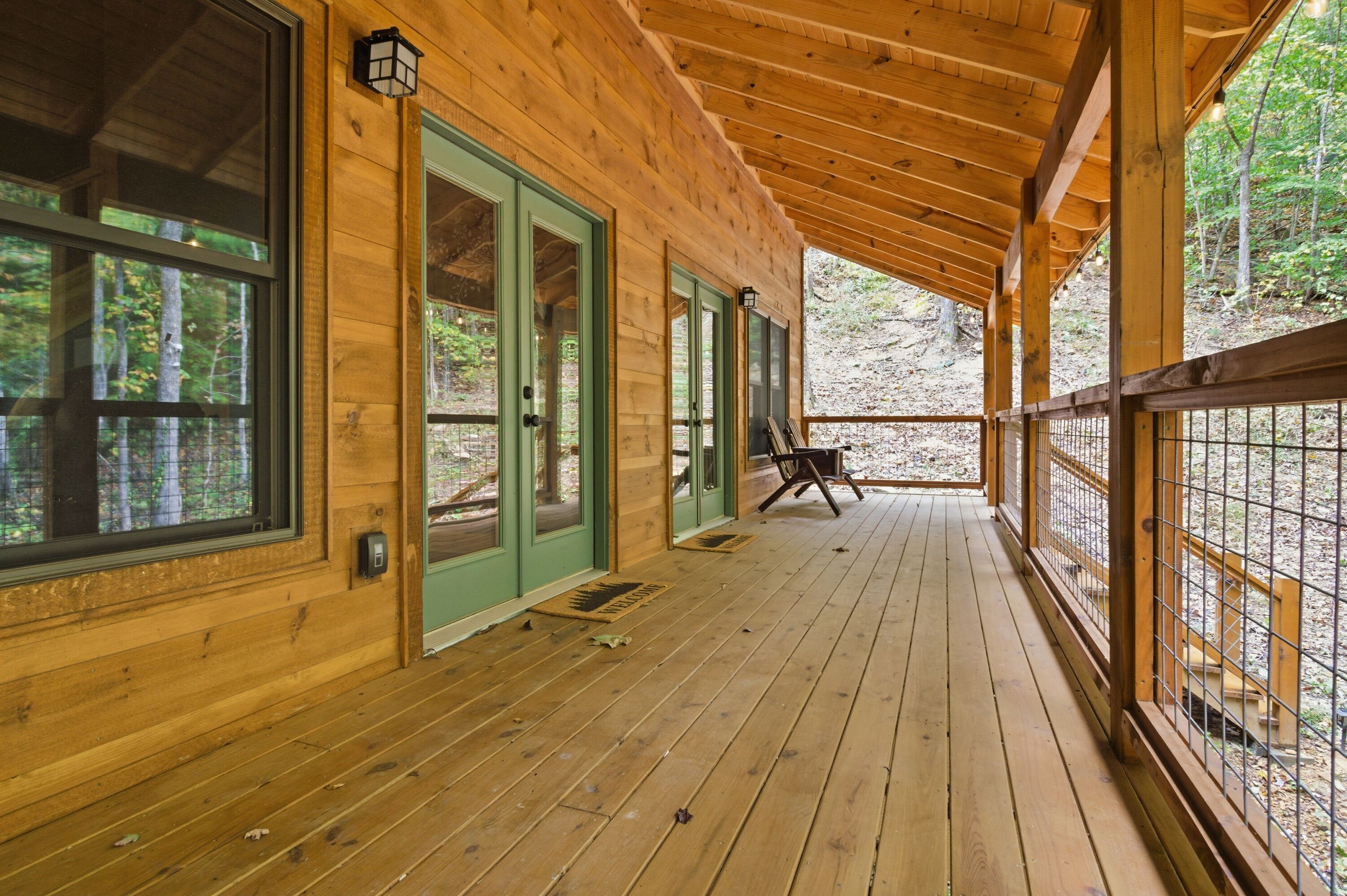 A wooden cabin with a covered porch, large windows, and a view of the forest.