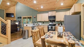 A modern kitchen with wooden cabinetry, a central island, and a dining area with rustic chairs. - Jones Creek Cove (Sevierville)