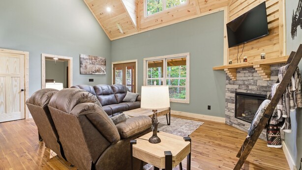A living room with a leather sectional sofa, a small table, a fireplace, and a TV mounted on a wooden wall. - Jones Creek Cove (Sevierville)