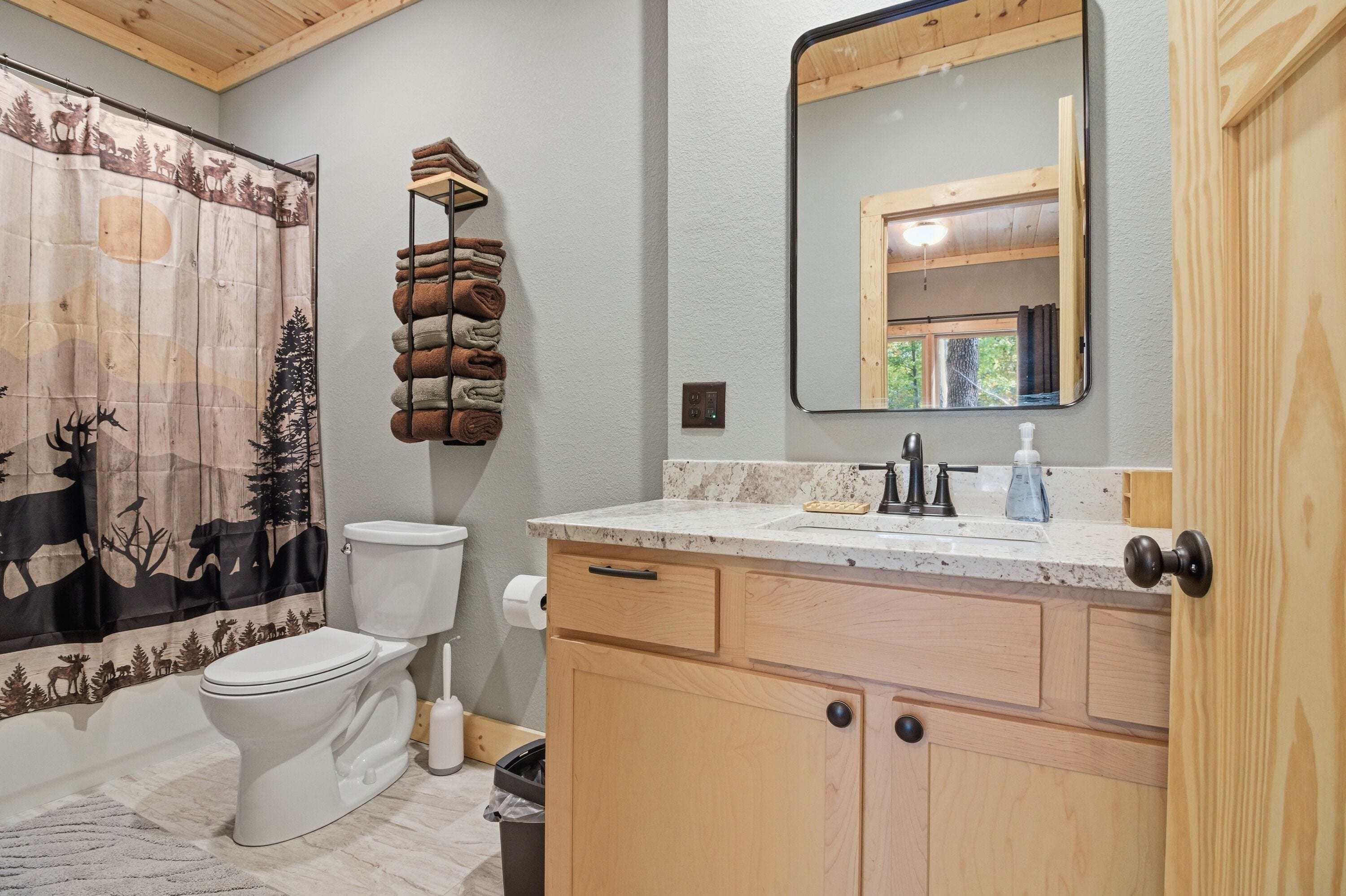 Un baño con inodoro, lavabo con espejo y cortina de ducha con diseño de bosque.