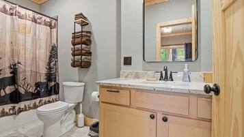 Un baño con inodoro, lavabo con espejo y cortina de ducha con diseño de bosque.