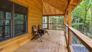 A wooden deck with two chairs and a table, overlooking a forested area. - Jones Creek Cove (Sevierville)