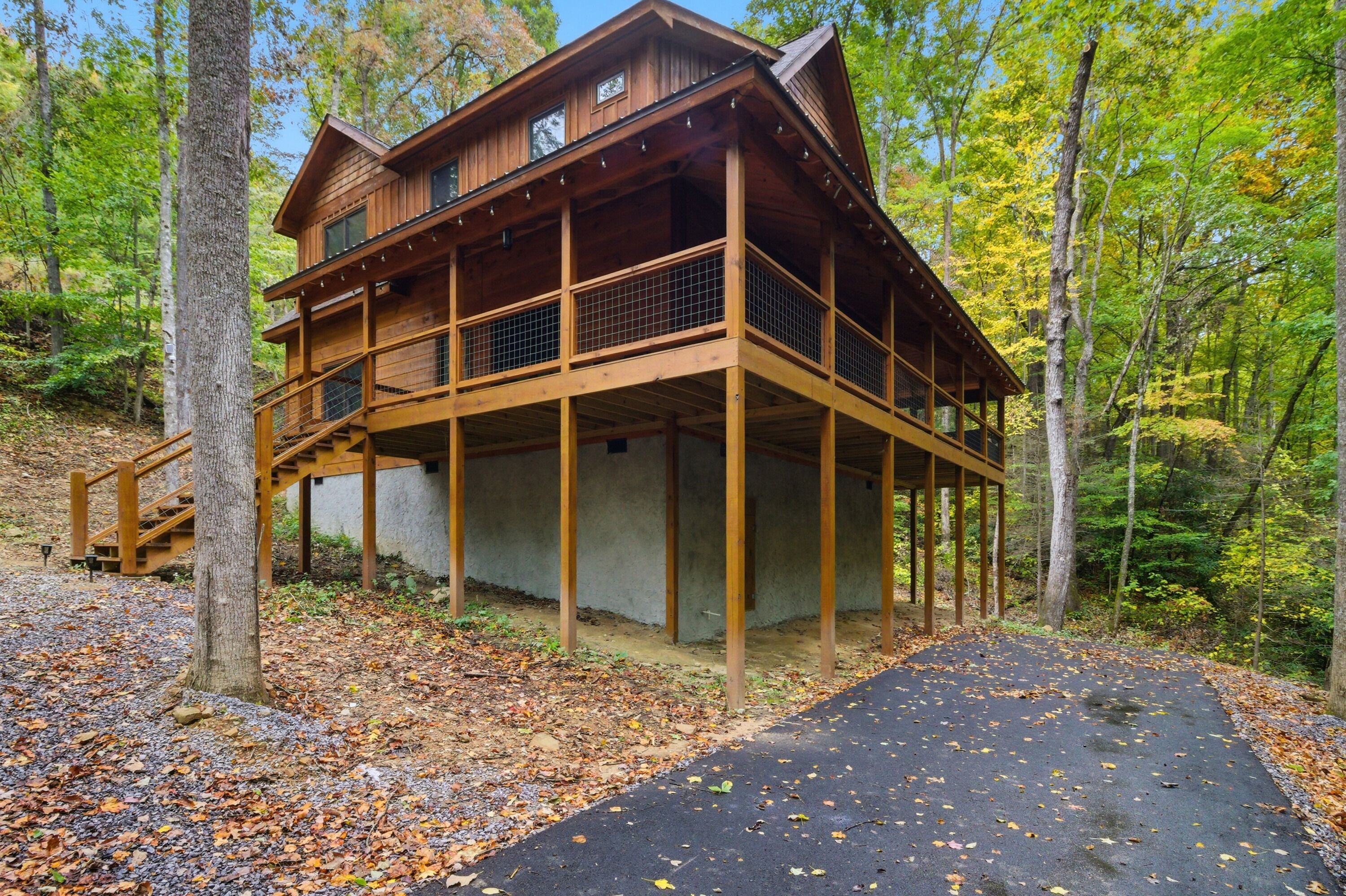 A two-story wooden cabin with a balcony, surrounded by trees and a gravel path.