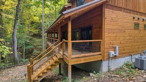 A wooden cabin with a covered porch, a staircase, and a view of the surrounding forest. - Jones Creek Cove (Sevierville)