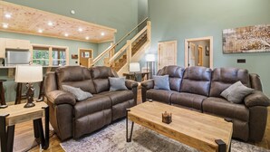 A spacious living room with two brown leather sofas, a wooden coffee table, and a staircase leading to an upper level. - Jones Creek Cove (Sevierville)