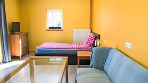 Une pièce de taille modeste comprenant un lit, un canapé, une petite table, une commode et une fenêtre.