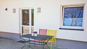 Une terrasse extérieure avec une table et des chaises, une fenêtre donnant sur un beau paysage et une porte.
