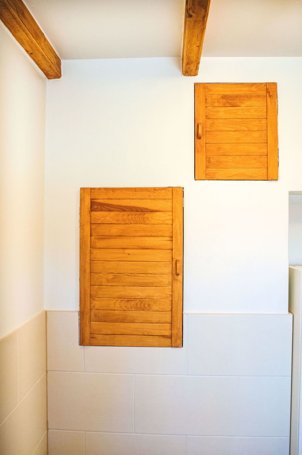 Un baño con paredes de azulejos blancos, vigas de madera y dos paneles de madera en la pared.