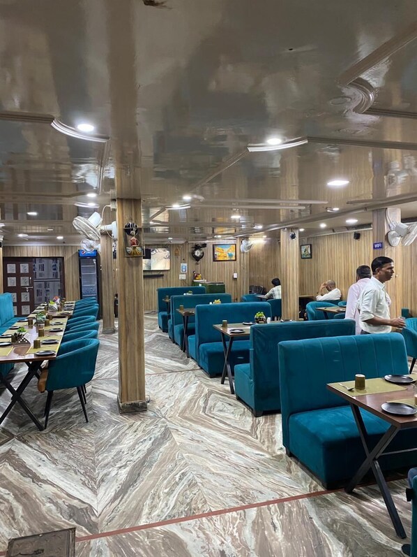 Un restaurante con suelo de mármol, asientos tapizados en azul y una larga mesa comedor común.