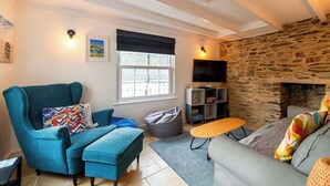A cozy living room with a stone fireplace, a blue sofa, a grey sofa, a blue armchair, and a small wooden table.