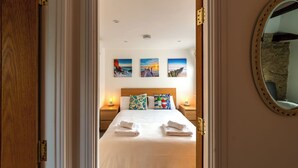 A hotel room with a neatly made bed, a wooden headboard, and three wall-mounted paintings depicting coastal scenes.