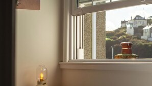 A bedroom with a bed, a bedside lamp, and a window with a view of houses and a chimney.