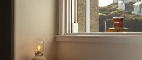 A bedroom with a bed, a bedside lamp, and a window with a view of houses and a chimney.