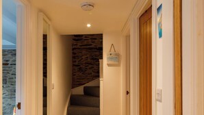 A narrow hallway with a stone wall, a wooden door, and a staircase with a grey carpet.