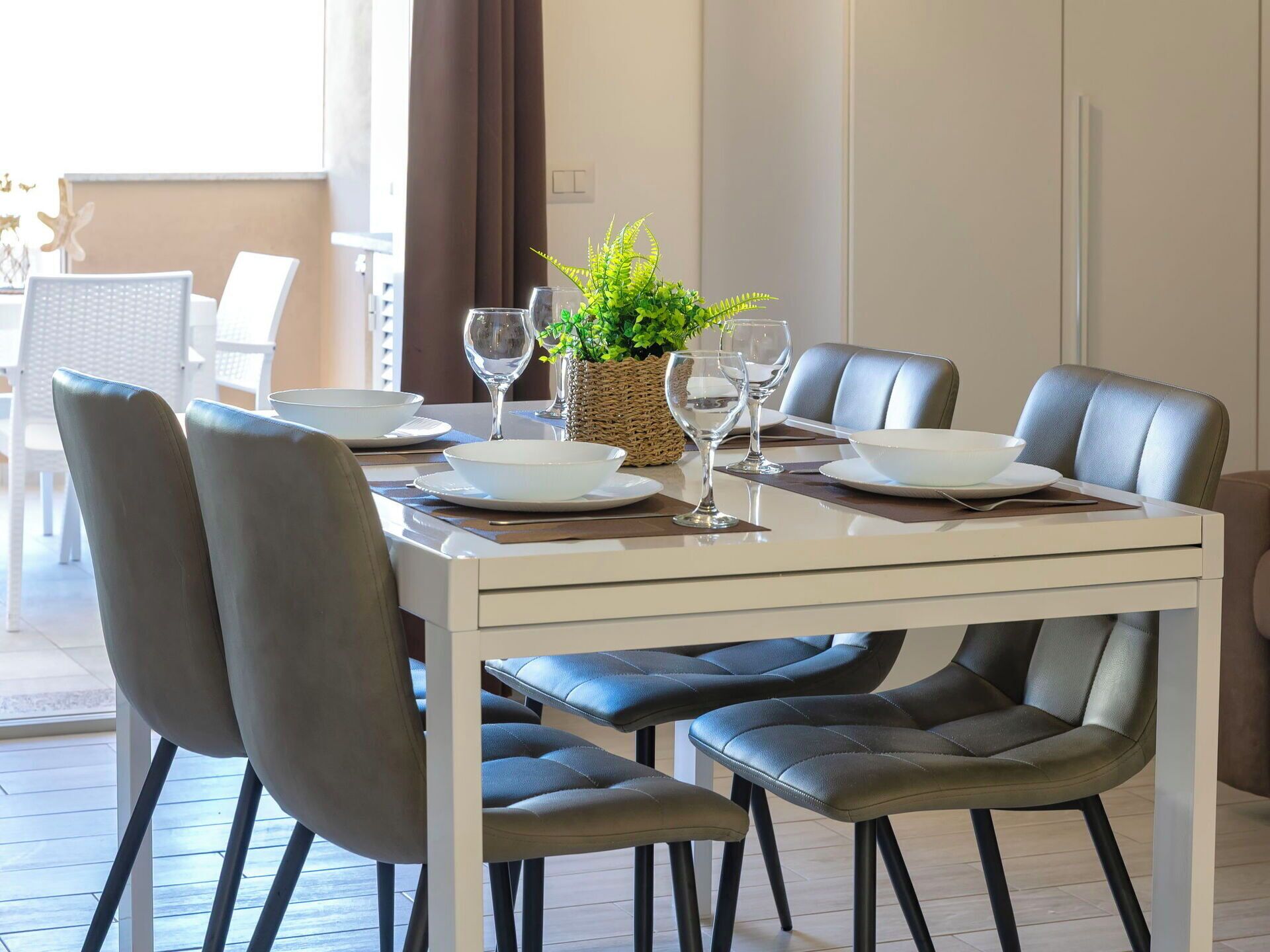 Uma sala de jantar com uma mesa branca posta para quatro pessoas, rodeada por cadeiras estofadas cinzentas.