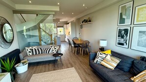 A modern living room with a sofa, a dining table, and chairs. There is a staircase leading to another level.