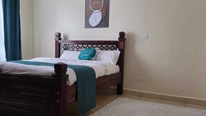 A neatly made bed with a wooden headboard, a teal throw blanket, and a pillow with a Bible verse.