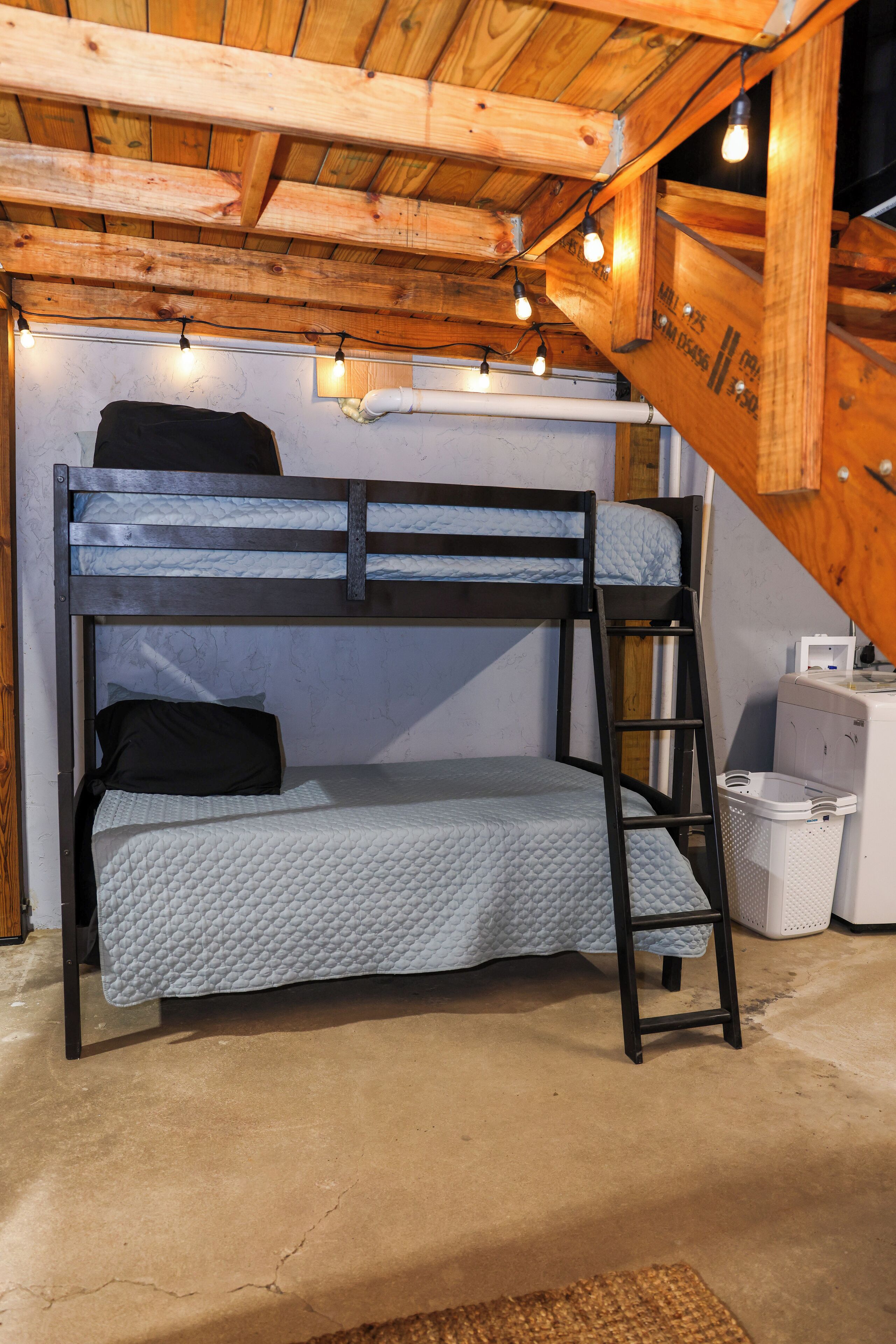 Una cama litera con escalera, una lavadora pequeña y un cubo de basura en una habitación de madera.