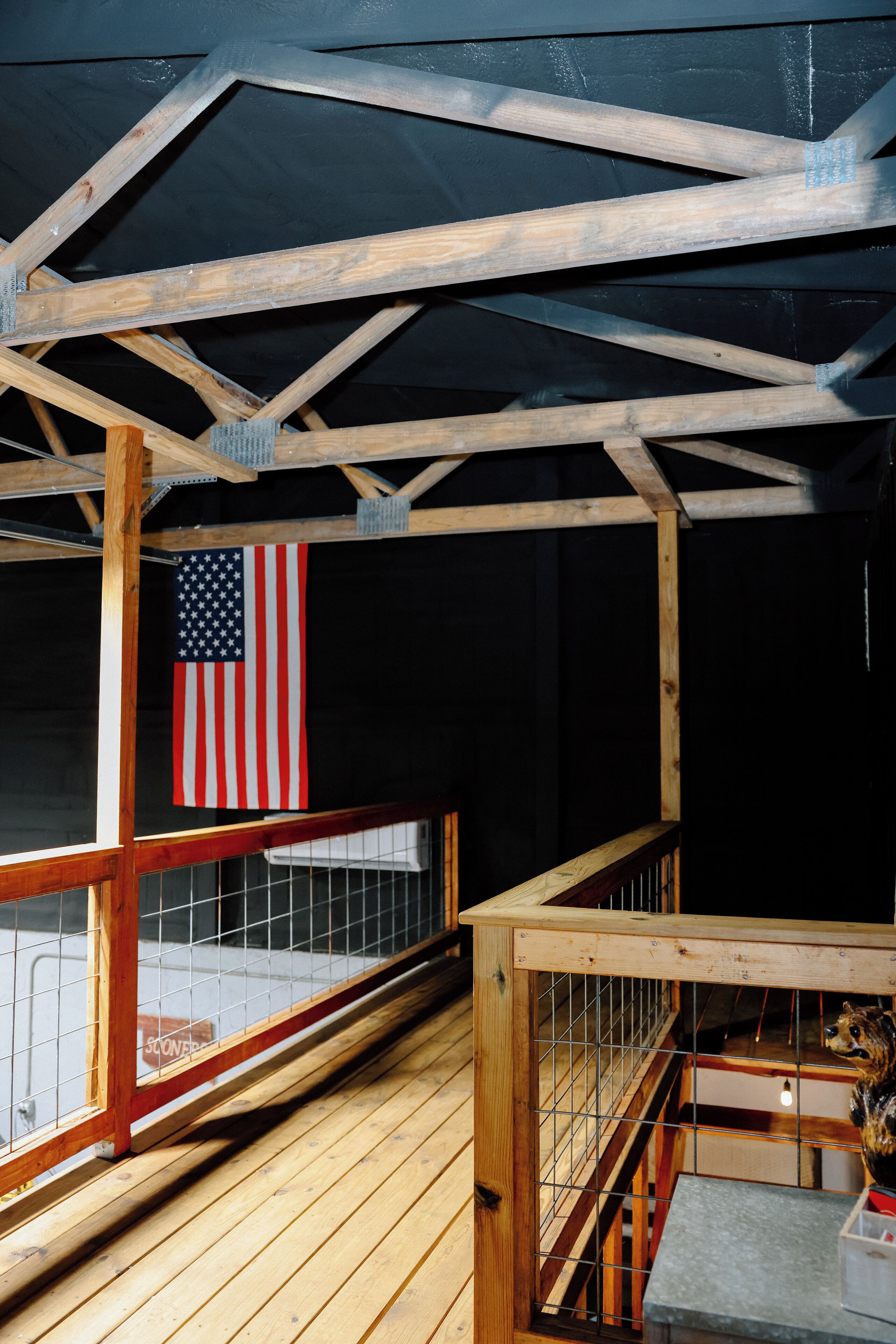A wooden deck with a metal railing, an American flag, and a view of a building through the railing.