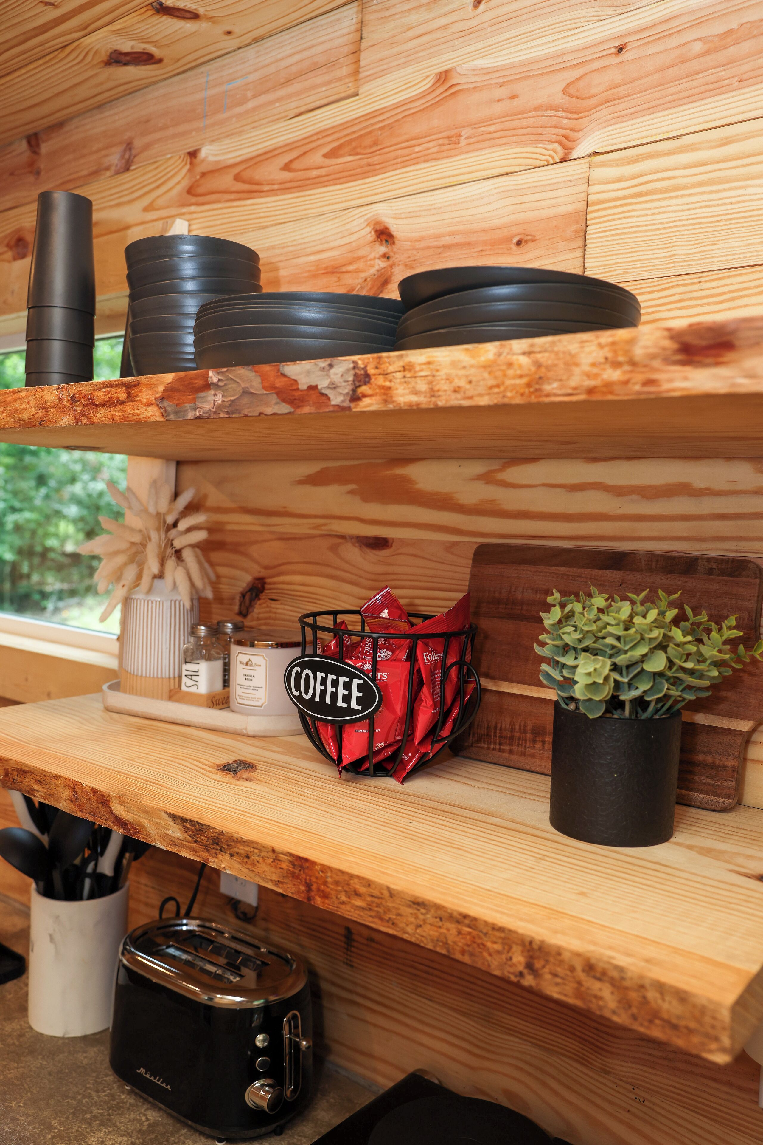 Una baldufa de fusta amb plats negres, un envasament de cafè, un torrador i una planta en test.