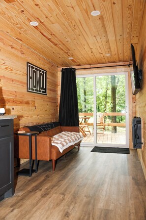 Interior acogedor de una cabaña con techo de madera, un sofá, una mesa de comedor y un ventanal corredero que da a una terraza exterior.