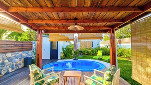 Ein überdachter Außenbereich mit Holzdeck, Swimmingpool und Gartenmöbeln.