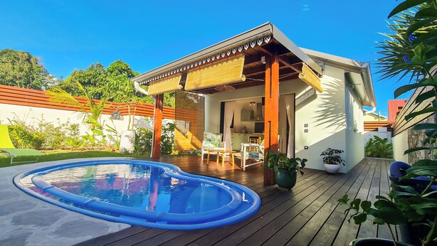 Ein modernes Haus mit einer Holzterrasse, einem Swimmingpool und einer überdachten Patio.