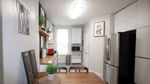 A compact kitchen with white cabinets, a stainless steel refrigerator, and a dining area with a wooden table and chairs. - 𖡡 Spring Suite in Hoboken - 1BR Apt - near NYC (Hoboken)