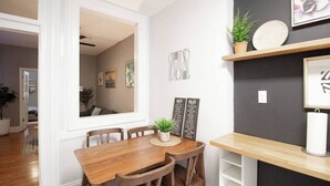 A dining area with a wooden table and chairs, a potted plant, and a wall-mounted menu board. - 𖡡 Spring Suite in Hoboken - 1BR Apt - near NYC (Hoboken)