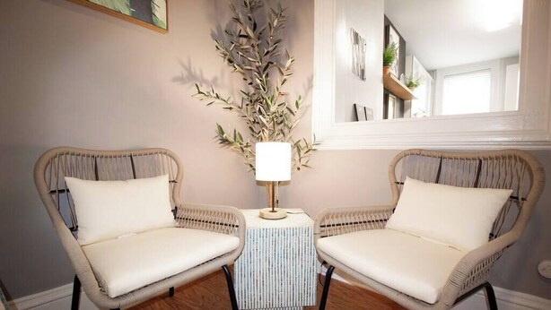 Two wicker chairs with white cushions, a small table with a lamp, and a tall decorative plant. - 𖡡 Spring Suite in Hoboken - 1BR Apt - near NYC (Hoboken)