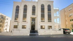 Un bâtiment à la façade symétrique, doté de grandes fenêtres en arc de cercle et d’une entrée centrale avec des marches.