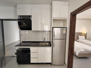 A compact kitchen with white cabinets, a black countertop, a stainless steel refrigerator, and a dishwasher.