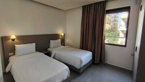 Une chambre d’hôtel avec deux lits, une fenêtre avec des rideaux et une vue sur les bâtiments environnants.