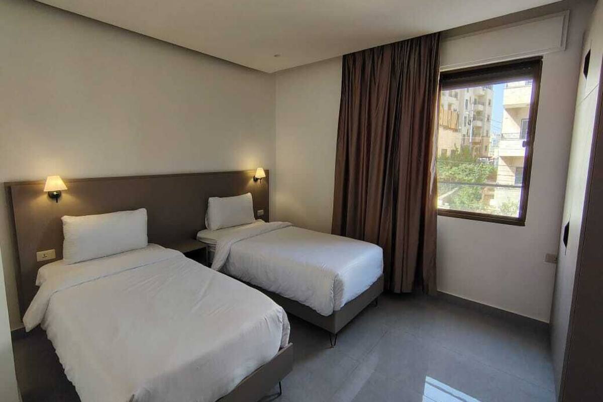 Een hotelkamer met twee bedden, een raam met gordijnen en uitzicht op gebouwen.
