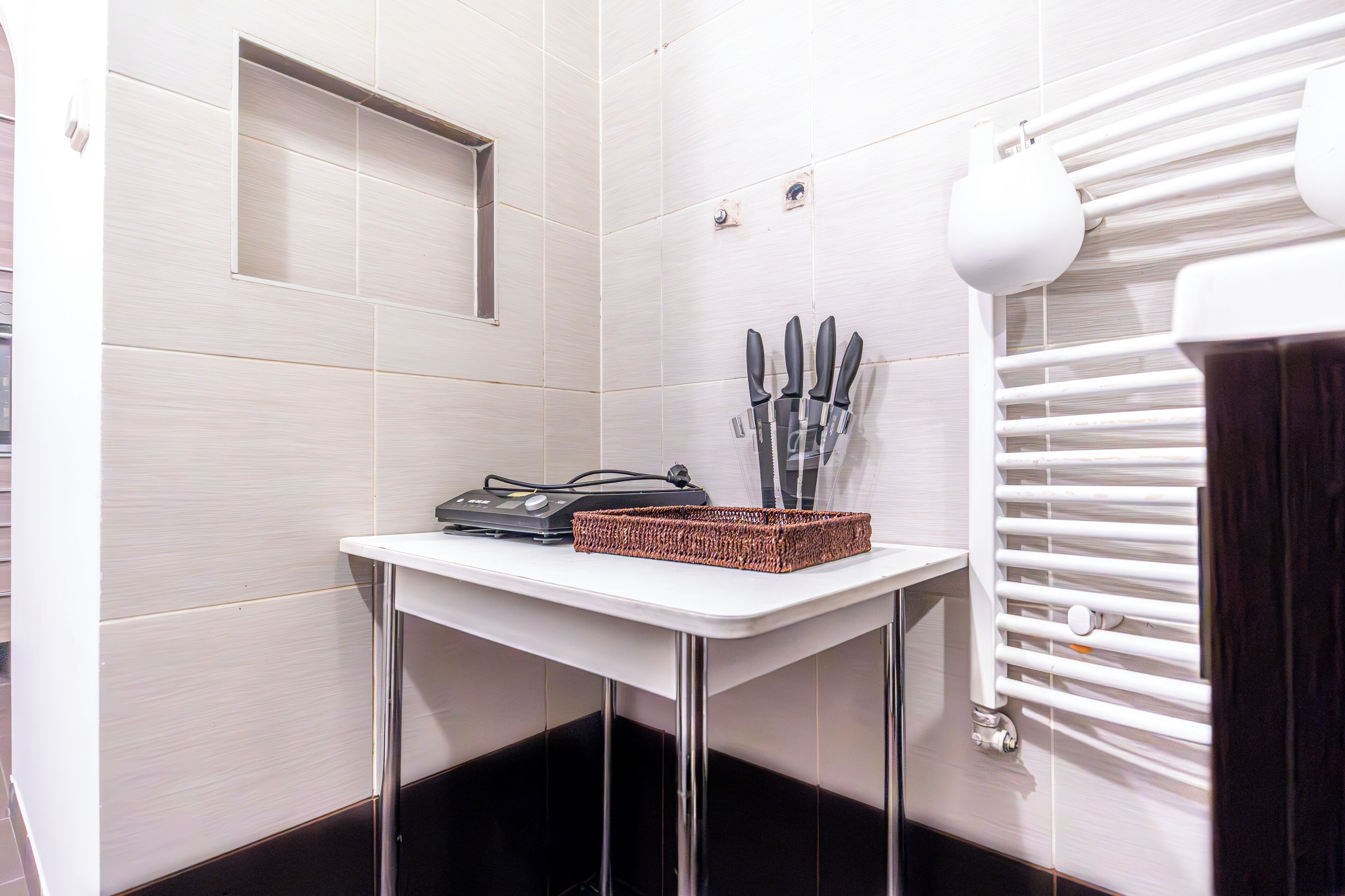 A bathroom with a white tiled wall, a small table with a basket, and a towel rack.