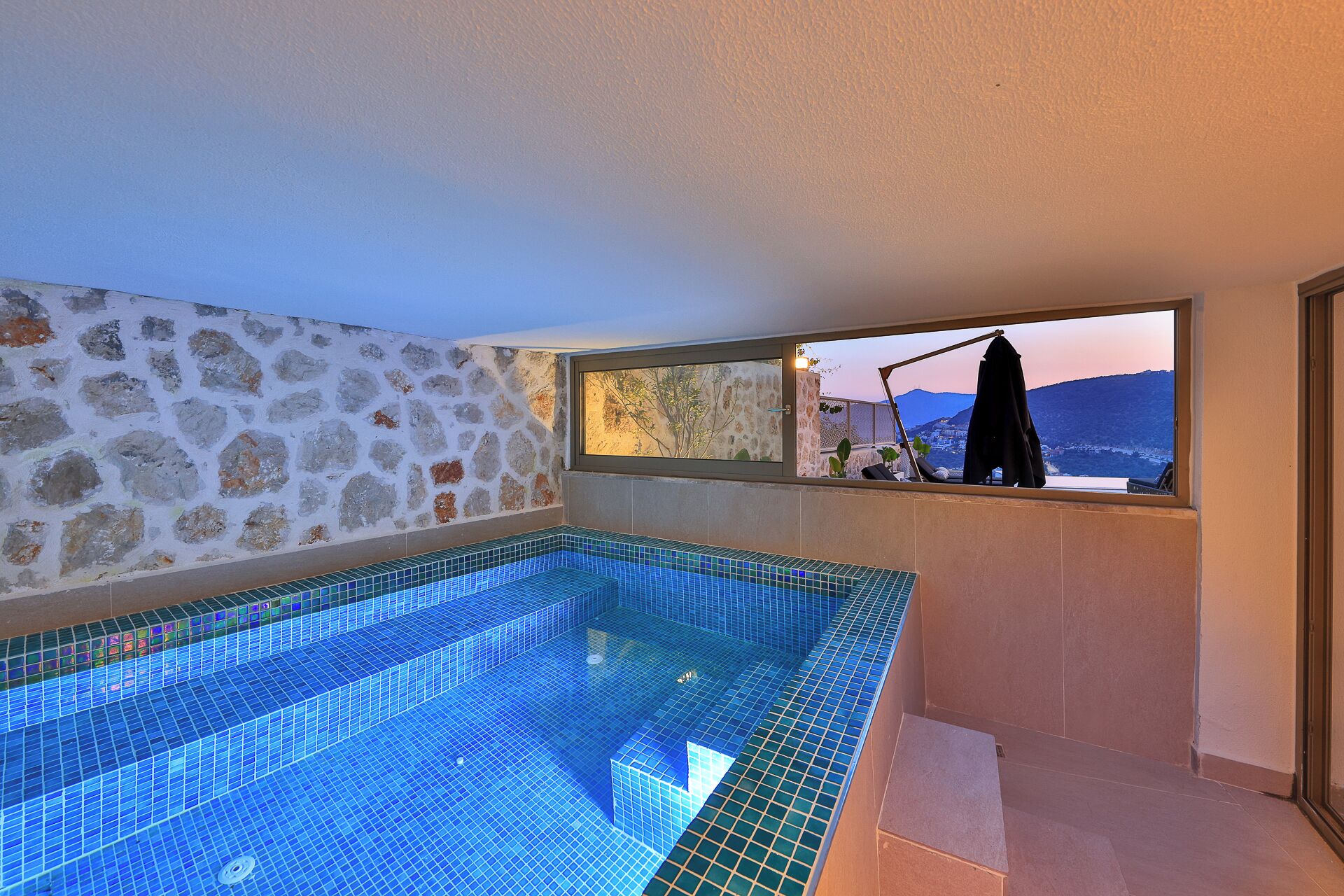 Une petite piscine intérieure, entourée de murs en pierre, avec une fenêtre donnant sur un paysage montagneux.